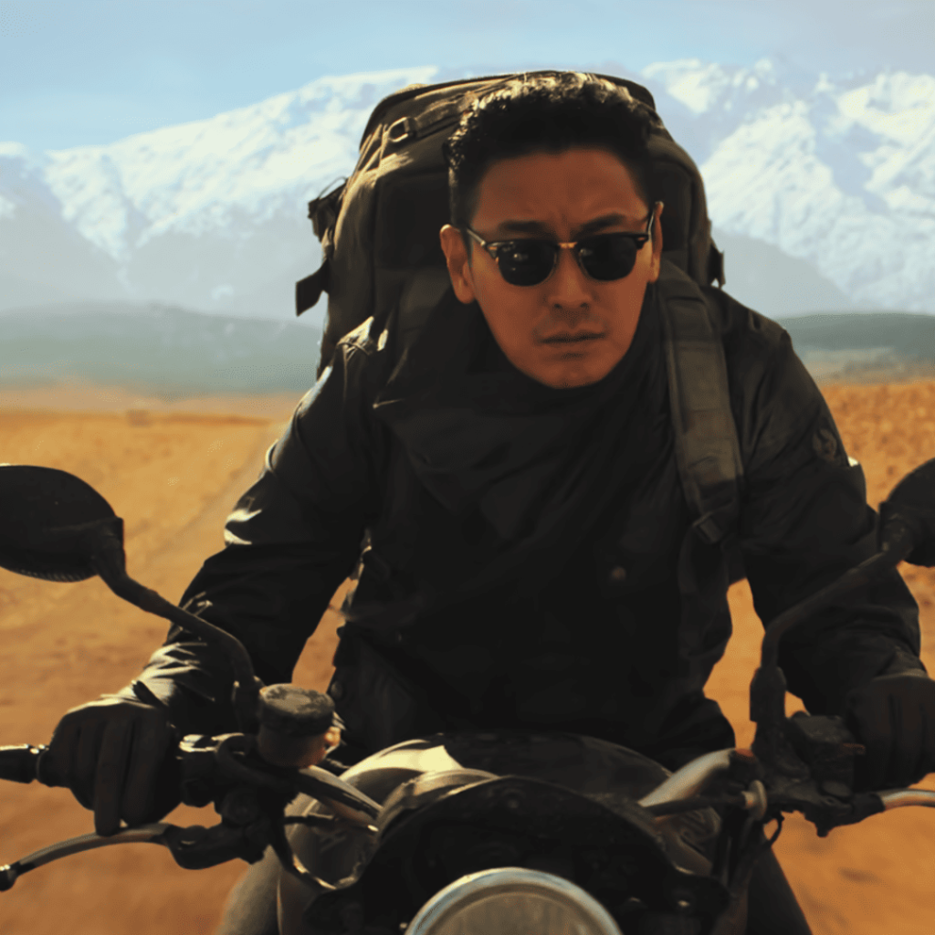 Trauma Code - a person in sunglasses riding a motorcycle with mountains in the background