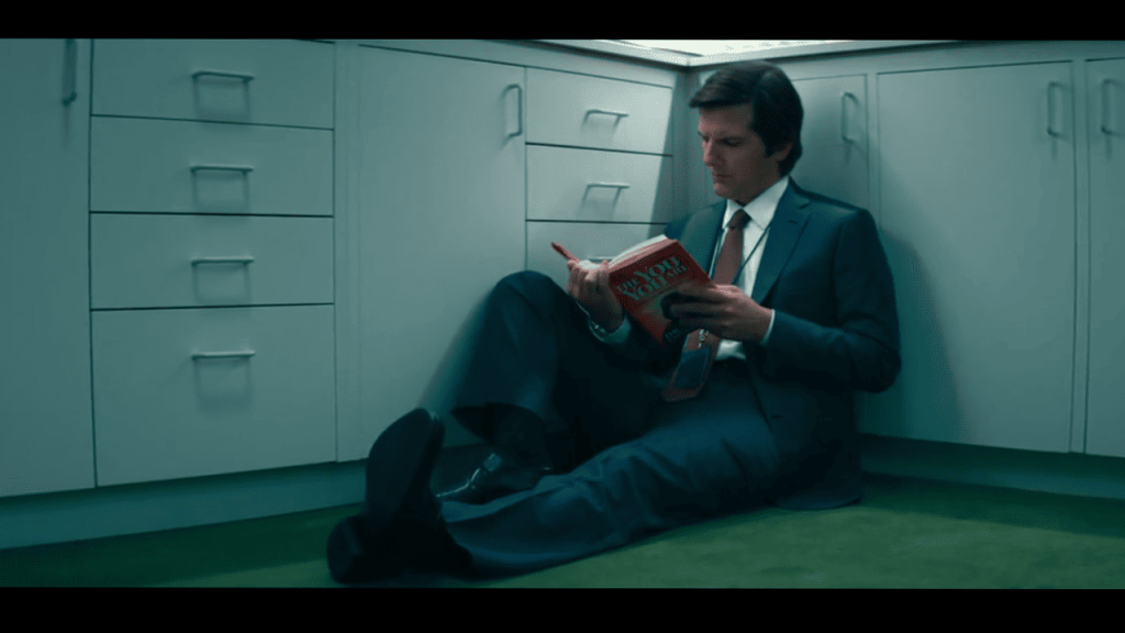Severance Season 1 Ending Explained: a person in a suit and tie sitting on the floor reading a book