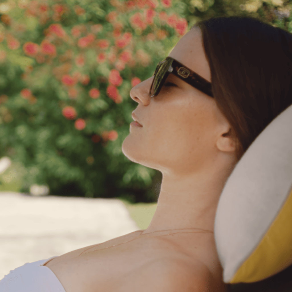 Delicious 2025 Review: A person in a white tank top and sunglasses is laying on a sun lounger.