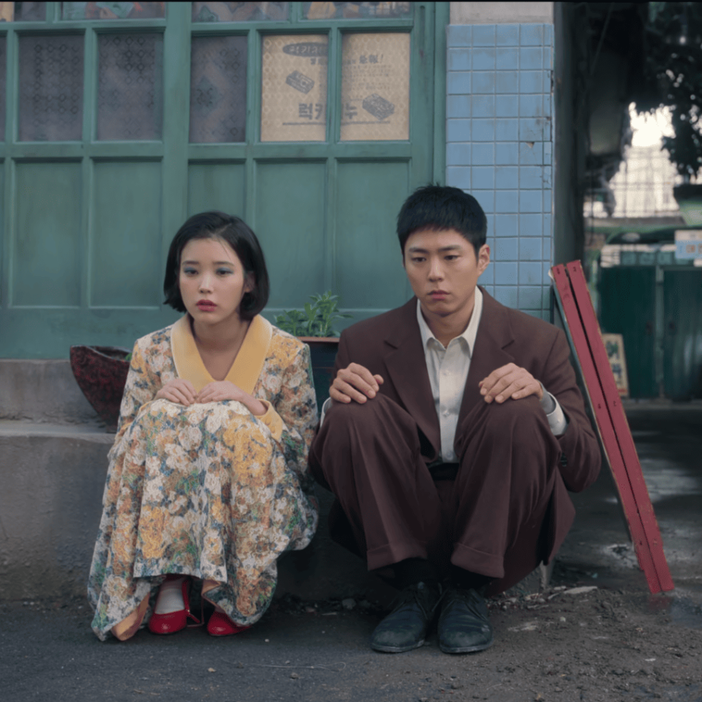 When Life Gives You Tangerines Review: Two individuals sitting on the ground next to each other.