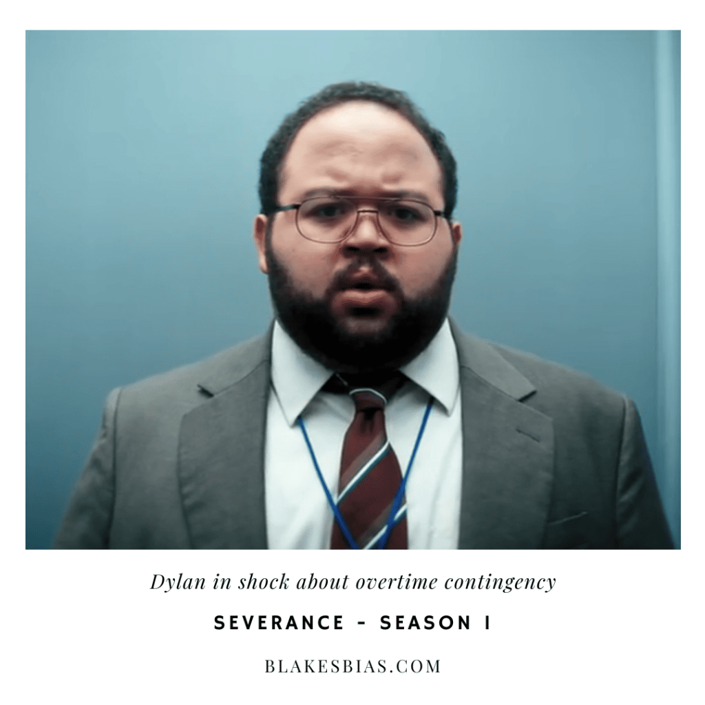 Best Severance Characters: A person in a suit and tie standing in front of a blue wall.