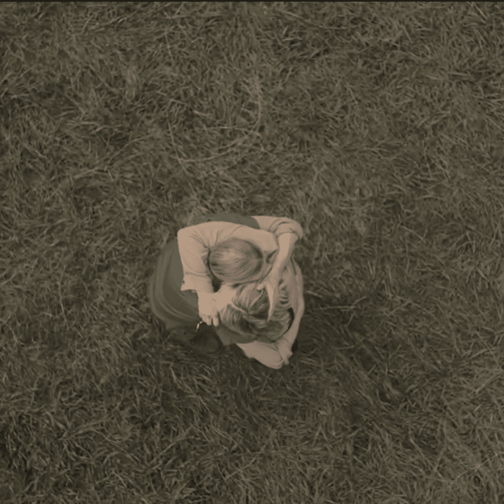 Overhead shot of June embracing her mother, their heads pressed together standing on the grass, a rare moment of peace in Handmaid’s Tale Season 6