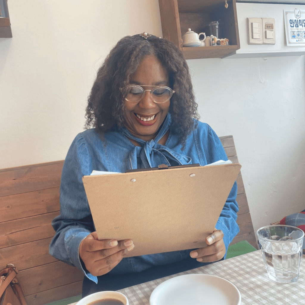 Decoding Humanity One Story at a Time: A person smiles while holding a clipboard at a table