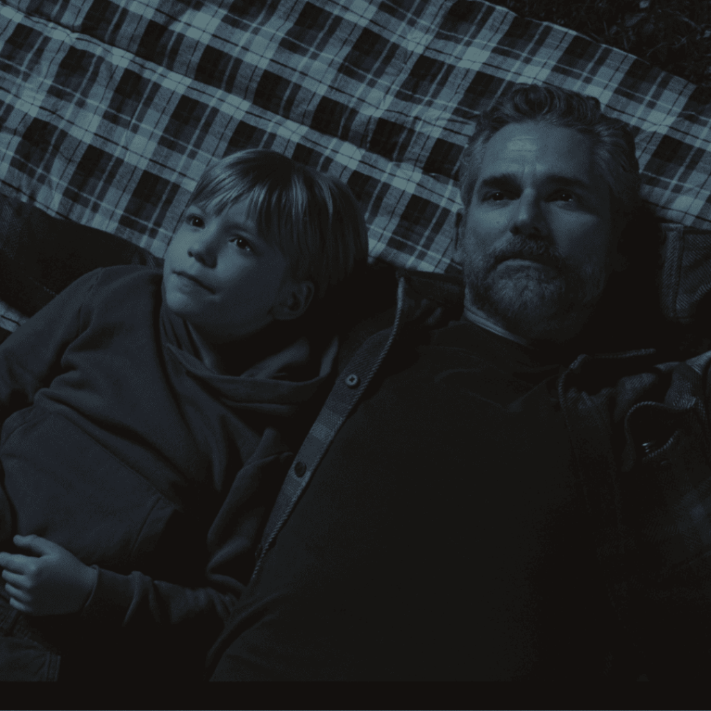 Untamed Netflix Review: In a black-and-white hallucination, Kyle sits under the stars with his late son Caleb, grief softening into a surreal moment of connection on a blanket in the woods.