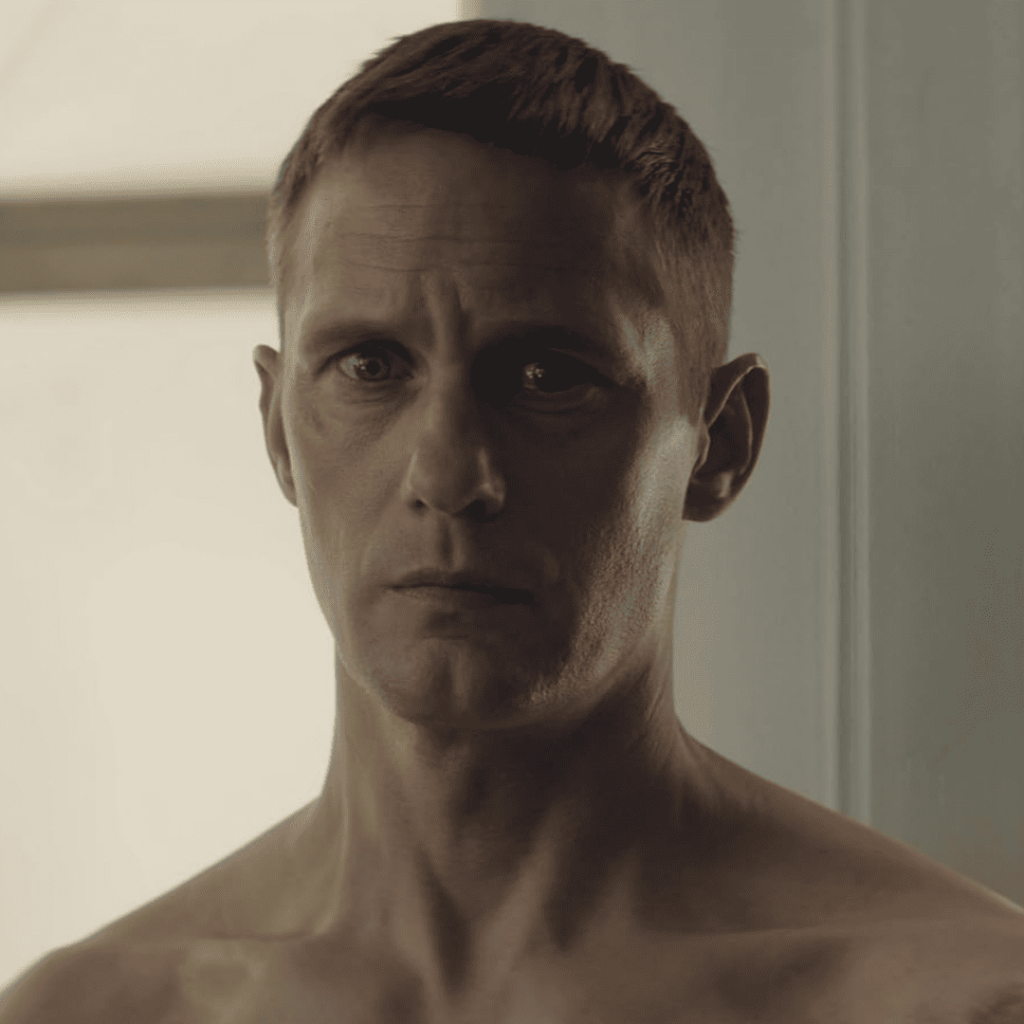 Murderbot Show Explained: Close-up of a shirtless, expressionless Murderbot staring blankly ahead, capturing his anti-human, deadpan vibe