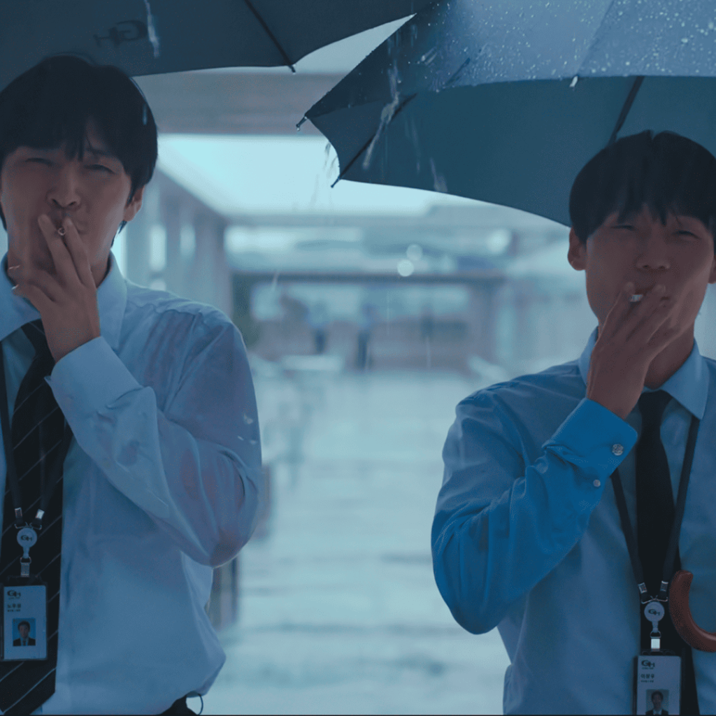 Two office workers smoke under umbrellas in the rain in Wall to Wall Movie Review.