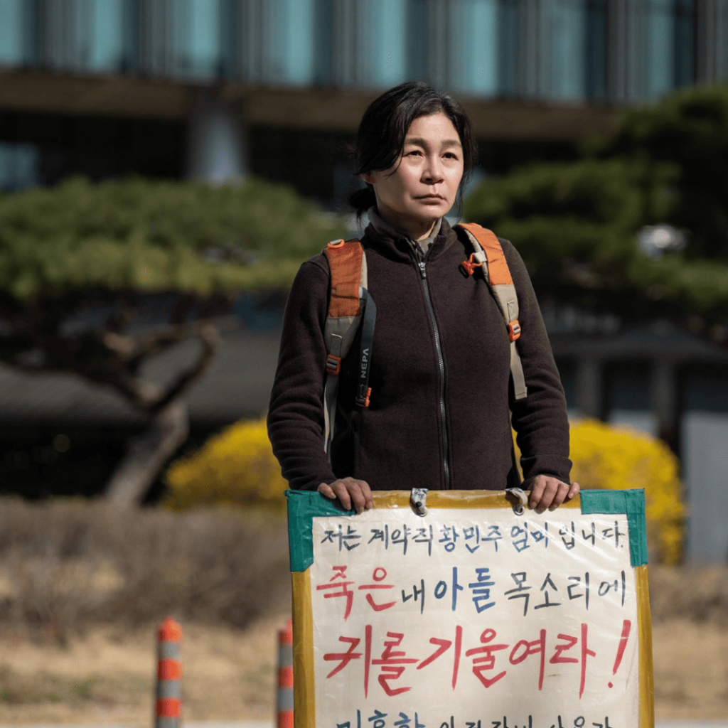 Kyung Sook holding a protest sign in Trigger K-drama Episodes 1-5 Review.