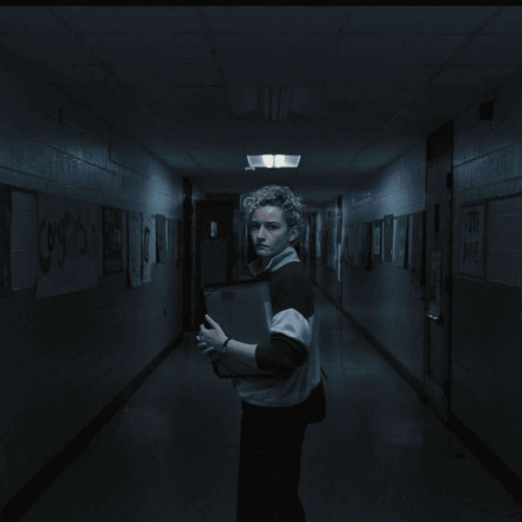 Weapons Movie Review image of Justine standing in a school hallway looking directly at the camera.