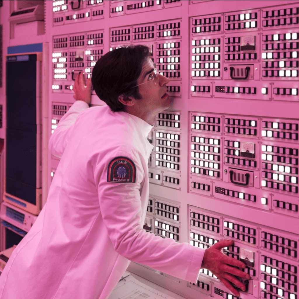 Maniac Review: Dr. James Mantleray leaning in to hug the massive, glowing GRETA supercomputer, a machine designed with a single large yellow "eye" sensor.