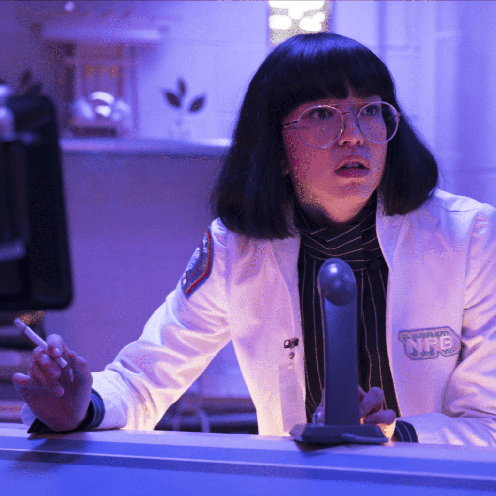 Maniac Review: A close-up shot of Dr. Azumi Fujita, with her signature short bob and glasses, staring intently while smoking a cigarette in a dimly lit lab.