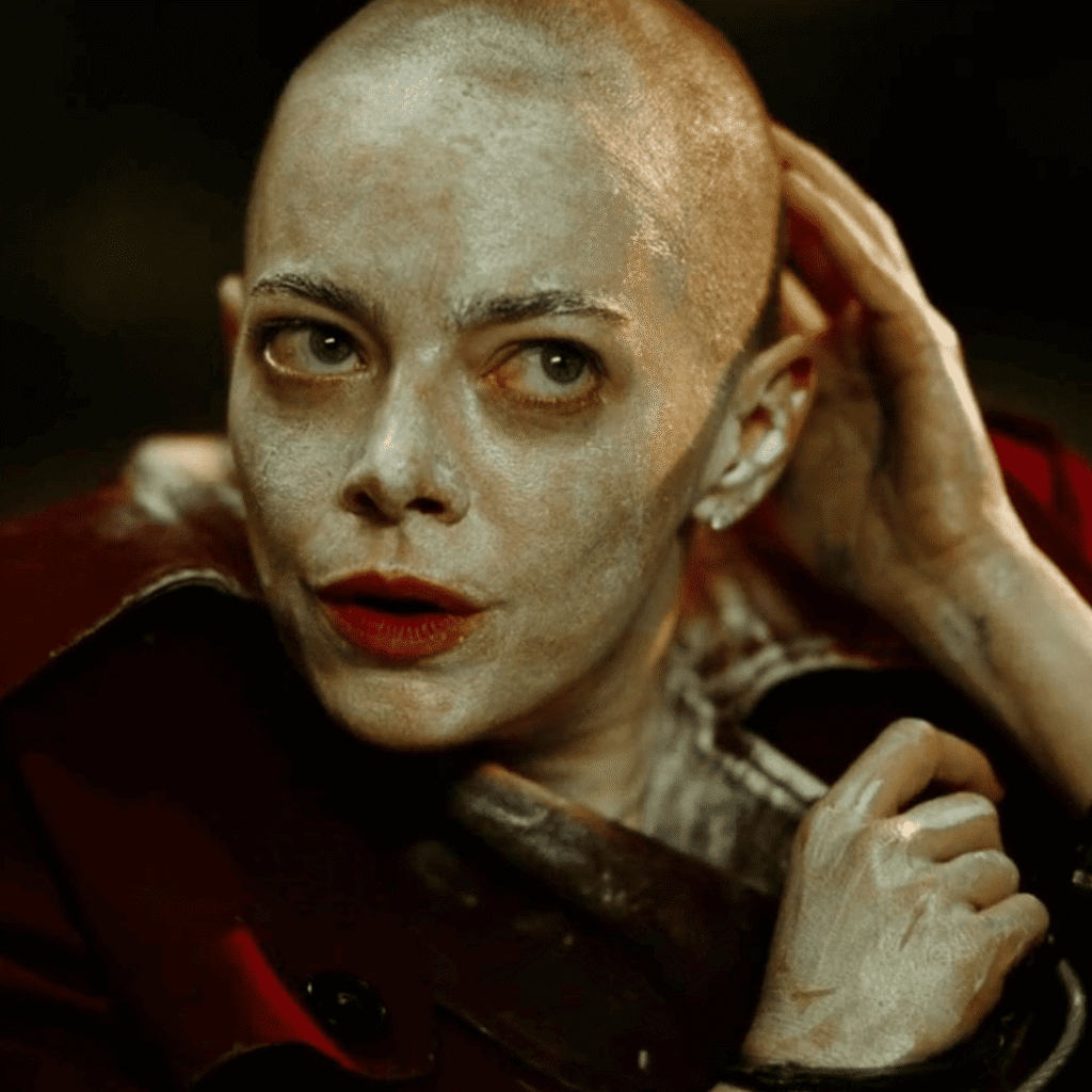 Bugonia Review: Close up of Michelle in Teddy’s basement with a shaved head coated in antihistamine cream and wearing a burgundy leather mac.