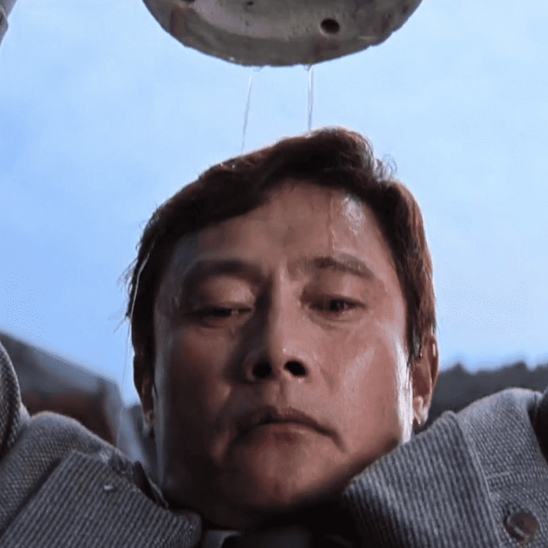 : A close up of Man-su on a rooftop for this No Other Choice Review holding a heavy vase above Choi Seon-chul.