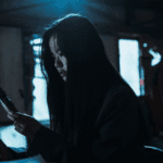 A dark, moody still for the If Wishes Could Kill Review FAQ showing Kim Si-won staring at the haunting glow of her mobile phone screen in a pitch-black room.