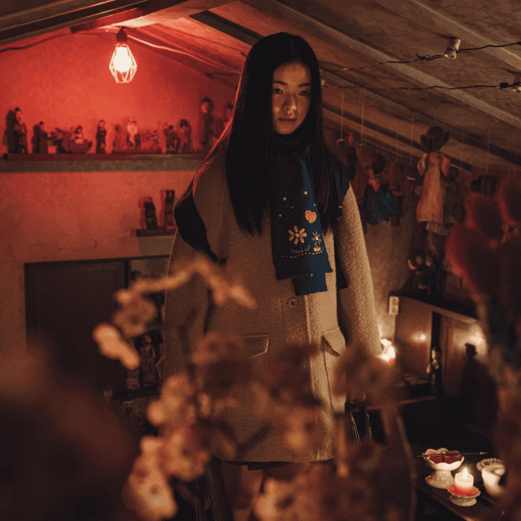 An atmospheric still for the If Wishes Could Kill Review of Hae-ryeong standing in Si-won’s mother’s attic, staring at the forbidden shamanic shrine.