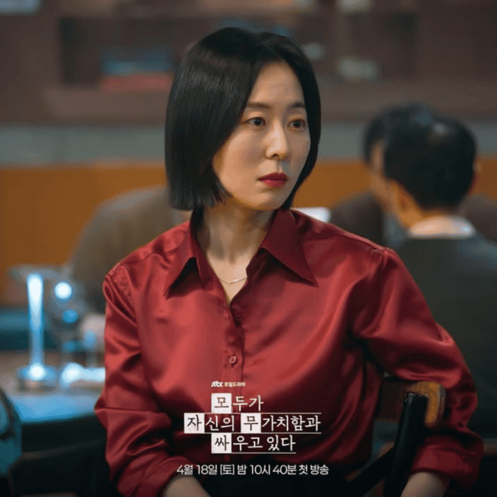 A production still for the We Are All Trying Here review released by JTBC, showing Kang Mal-geum as Ko Hye-jin sitting elegantly in her bar establishment while wearing a rich red satin shirt.