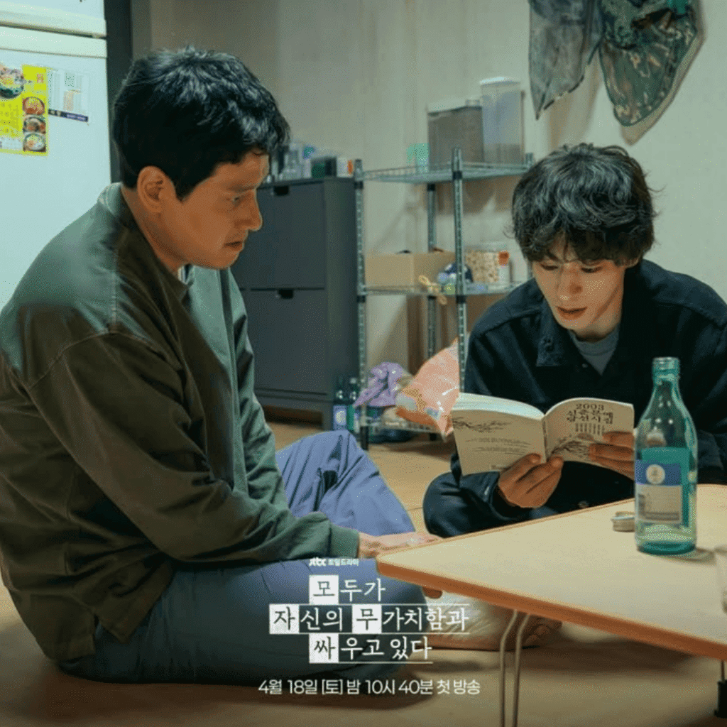 A production still for the We Are All Trying Here review released by JTBC, howing Hwang Dong-man holding an old poetry collection and reading his brother Jin-man's favorite verse aloud to him during a crisis.