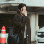 : A close-up dramatic still for the We Are All Trying Here review capturing Go Youn-jung as Byeon Eun-ah pressing a white handkerchief to her nose to stem a severe nosebleed.