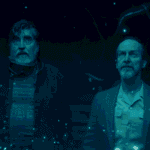 Sam and Wally standing in the middle of Sam's living room looking at the display left behind by the exploding alien DNA for The Boroughs Review.