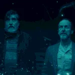Sam and Wally standing in the middle of Sam's living room looking at the display left behind by the exploding alien DNA for The Boroughs Review.