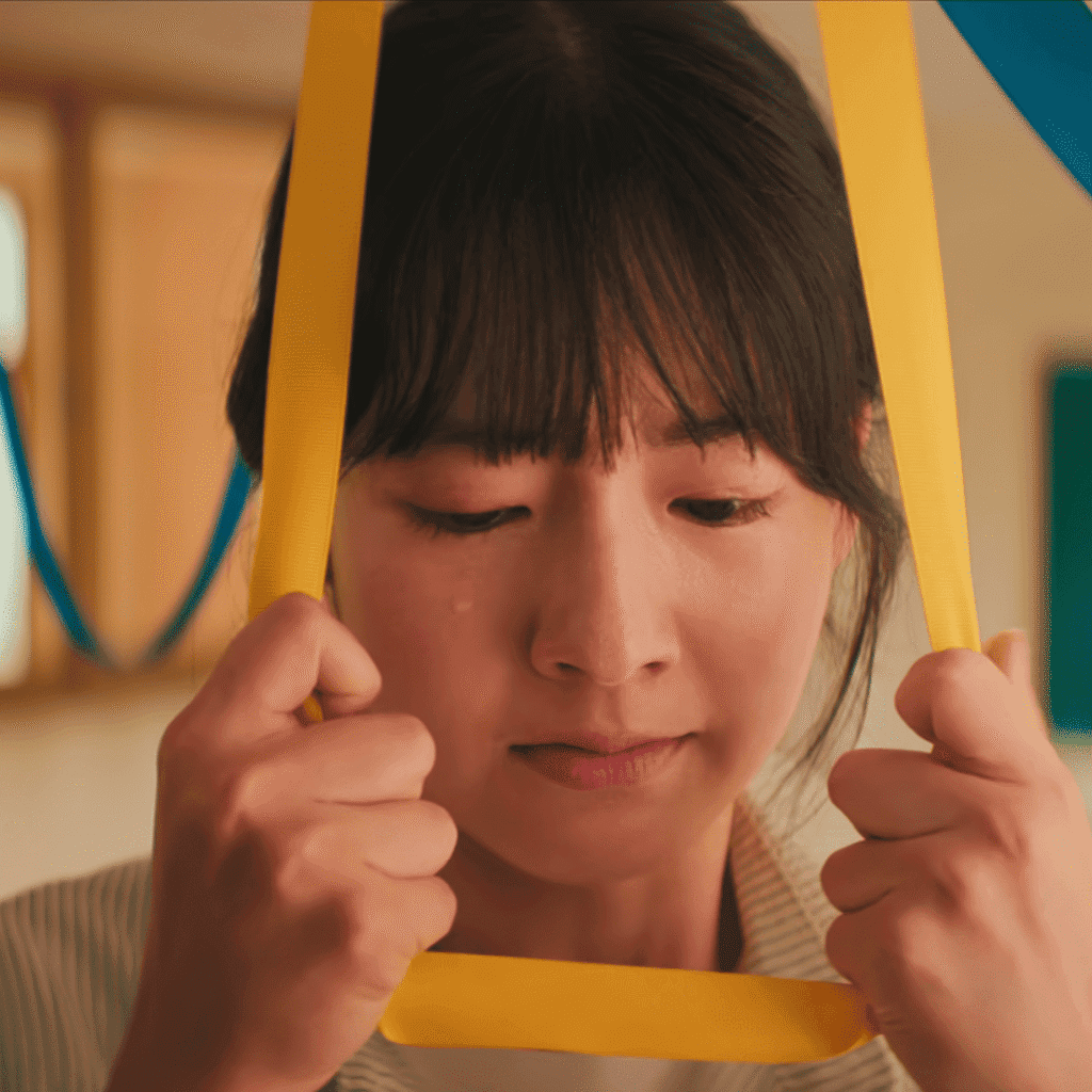 A tragic dramatic still from our Teach You a Lesson review showing a female teacher near a yellow ribbon after facing relentless parent harassment.