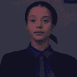 A close-up still image of Agnes dressed as a Plum Girl standing on the staircase inside her home for The Testaments Review.