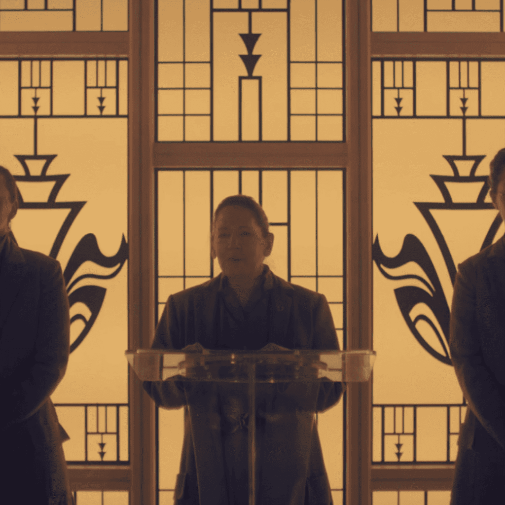 : A still image featuring Aunt Lydia standing in between two other aunts during Agnes's coming of age ceremony for The Testaments Review.
