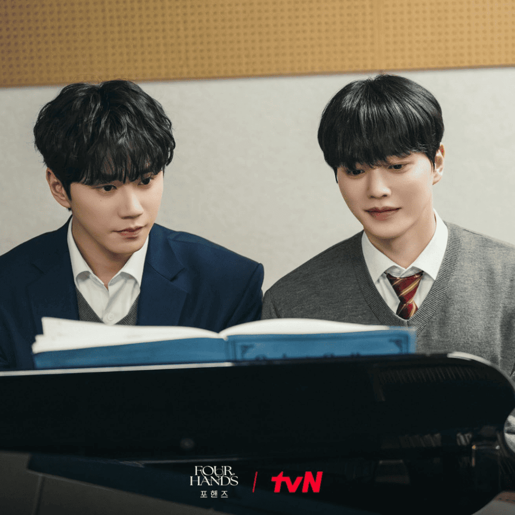 Official tvN still of Kang Pi-o and Choi Jeong-yo sitting side by side at a piano in school uniforms and reading sheet music in Four Hands, Two Sonatas.