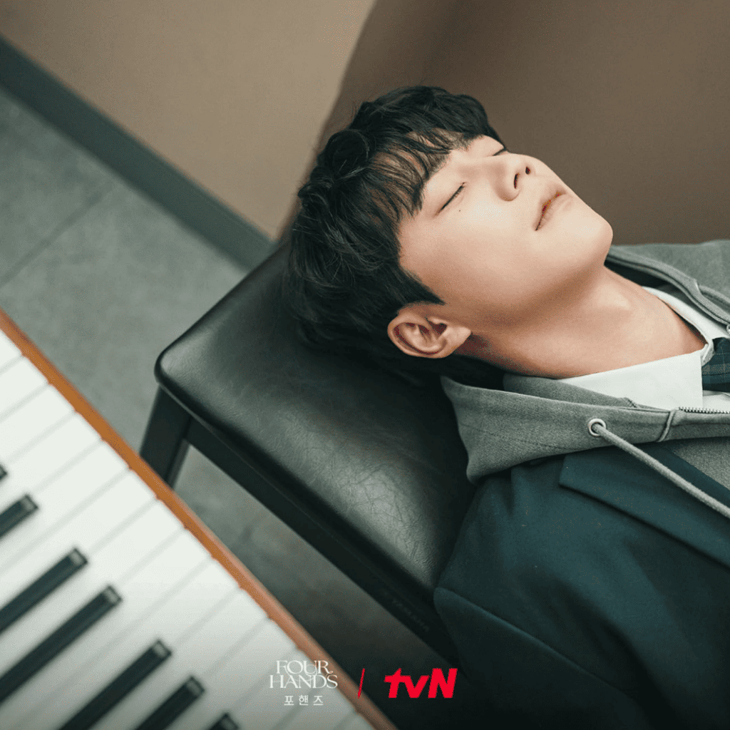 Official tvN still of Choi Jeong-yo with his eyes closed, reclining on the seat in front of a piano in Four Hands, Two Sonatas.
